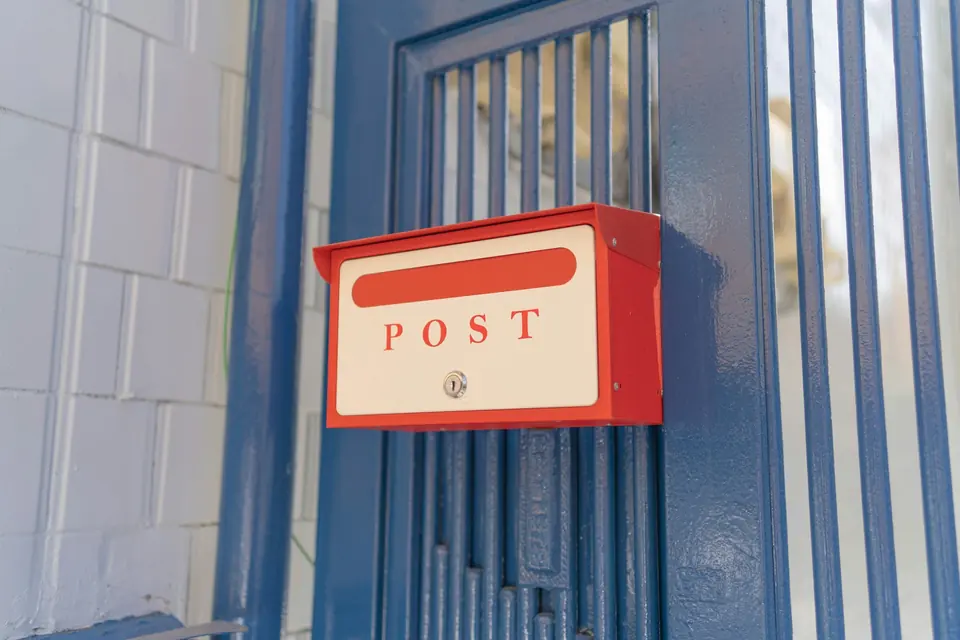 Rød postkasse med teksten POST montert på en blå jerndør