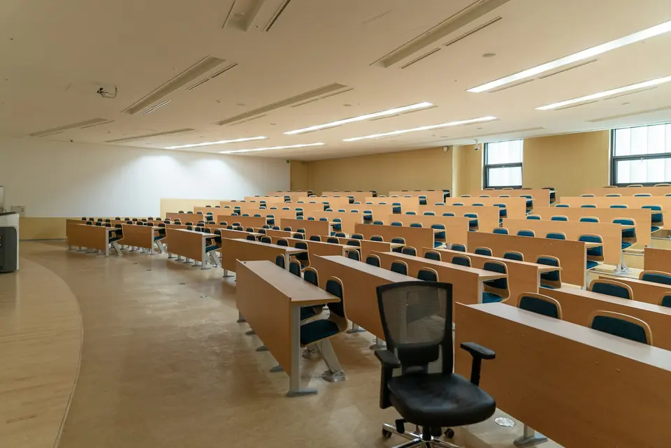 Tomt auditorium med rader av pulter og stoler i lyst tre